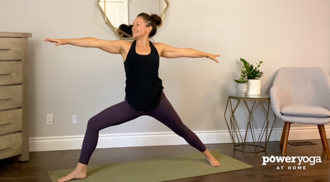 A woman doing a Warrior yoga pose in her living room